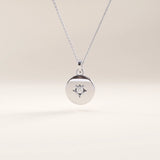 Silver vermeil starburst coin necklace with a sleek circular medallion showcasing a delicate starburst detail centered by a clear cubic zirconia stone.

